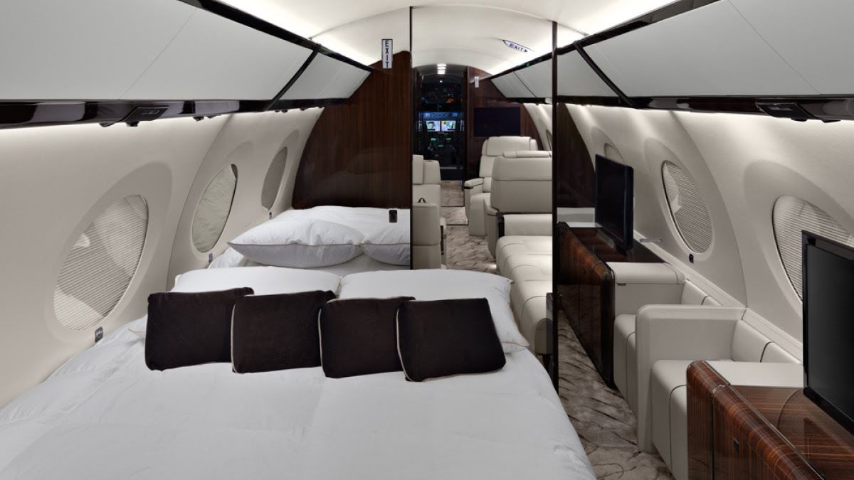 luxurious interior of a private jet with a bed, sofa and dark wood furniture accents