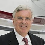 Portrait of Roger Whyte smiling in a black suit in front of a striped aircraft